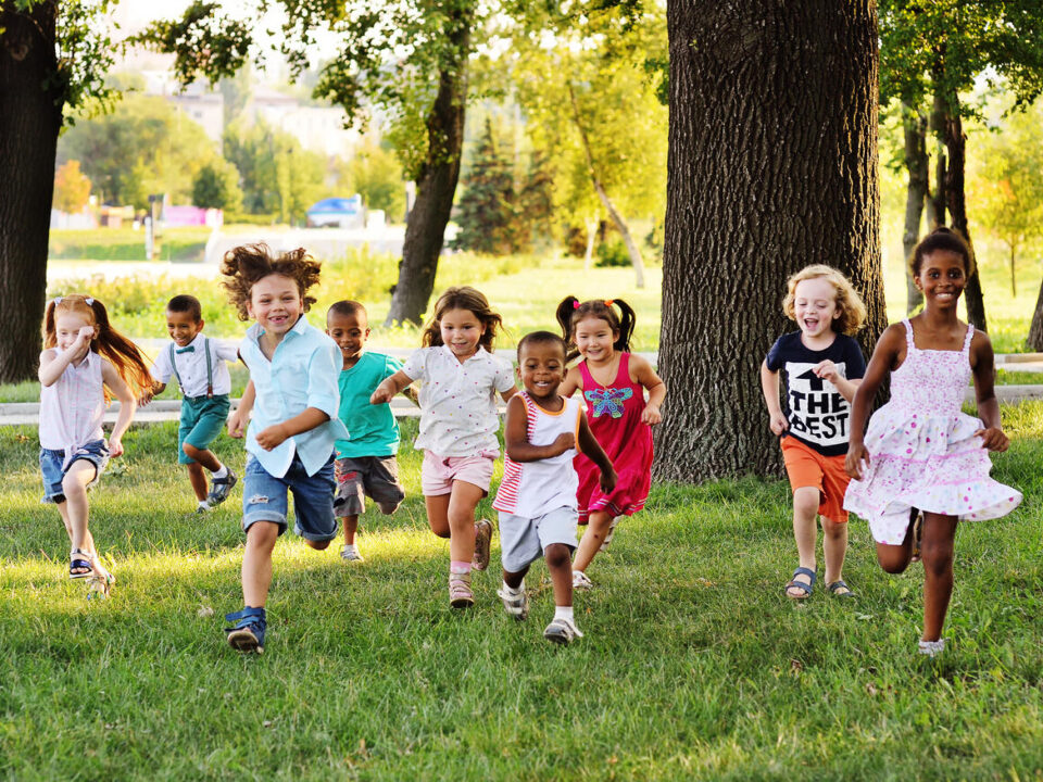 a group of preschoolers running on the grass in the Park