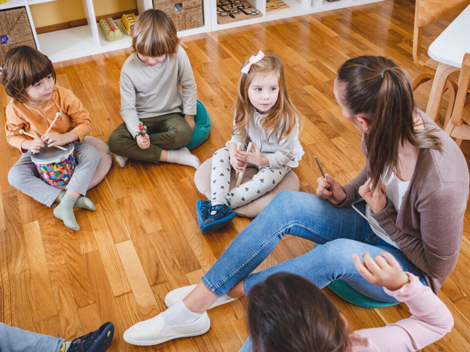 Kindergarten teacher with children sitting on the floor having music class, using various instruments and percussion.